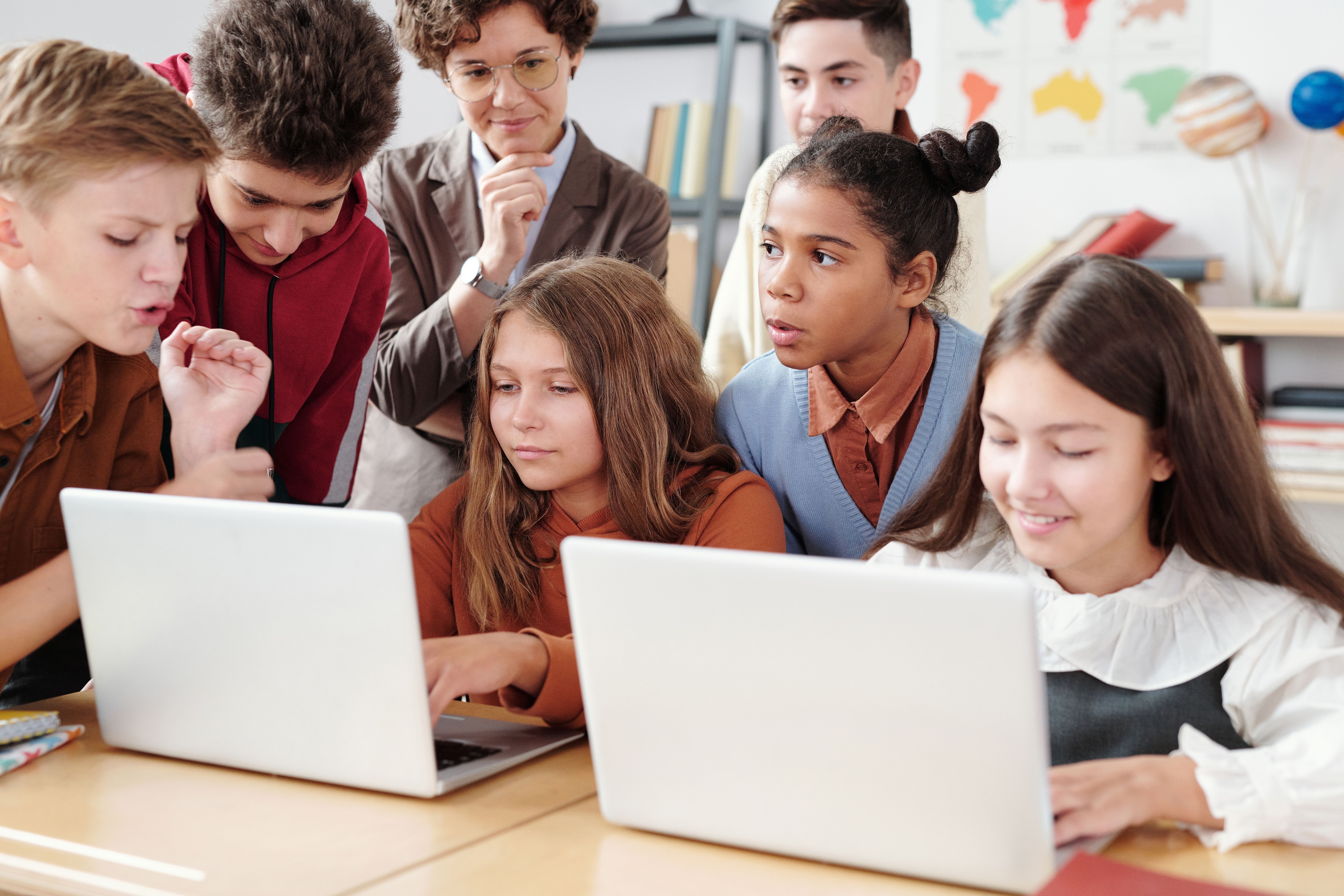Dos estudiantes usando un portátil junto a sus compañeros de clase en un aula con tecnología.